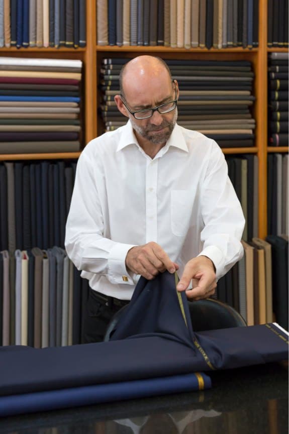 Tailor unrolling navy cloth in front of shelves stacked with suiting fabrics