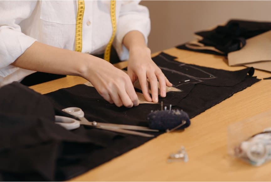 Hands chalk-marking black cloth on the cutting table
