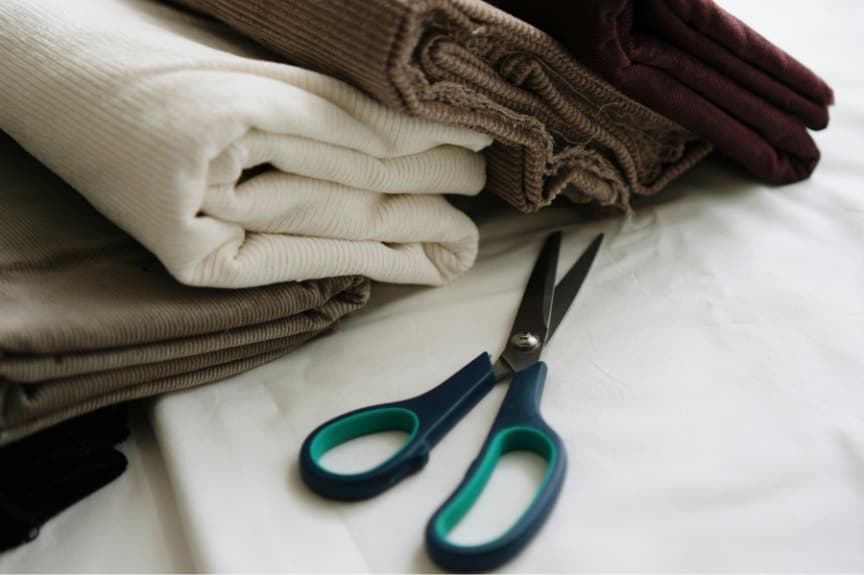 Folded fabrics in cream, taupe and burgundy beside a pair of scissors