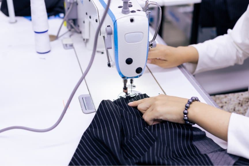 Seamstress guiding pinstripe cloth under an industrial sewing machine