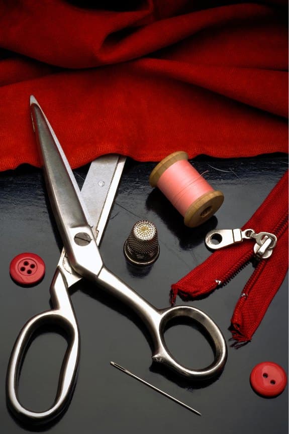 Tailor's shears, thimble and thread beside folds of red cloth