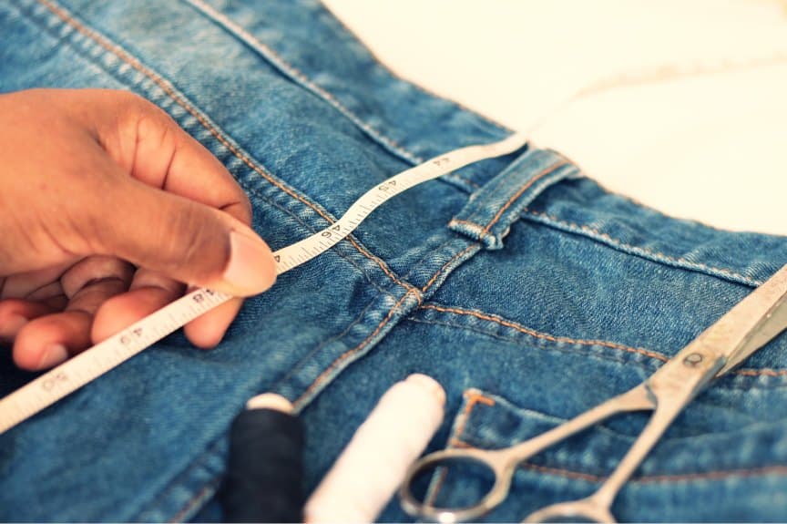 Tailor measuring the waistband of jeans with scissors and thread at hand