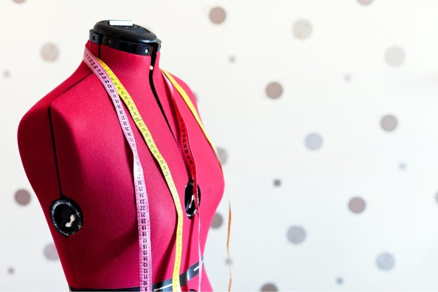 Bright pink dress form draped with colourful measuring tapes