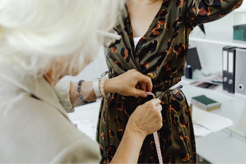 Dressmaker fitting a patterned dress on a client with a measuring tape