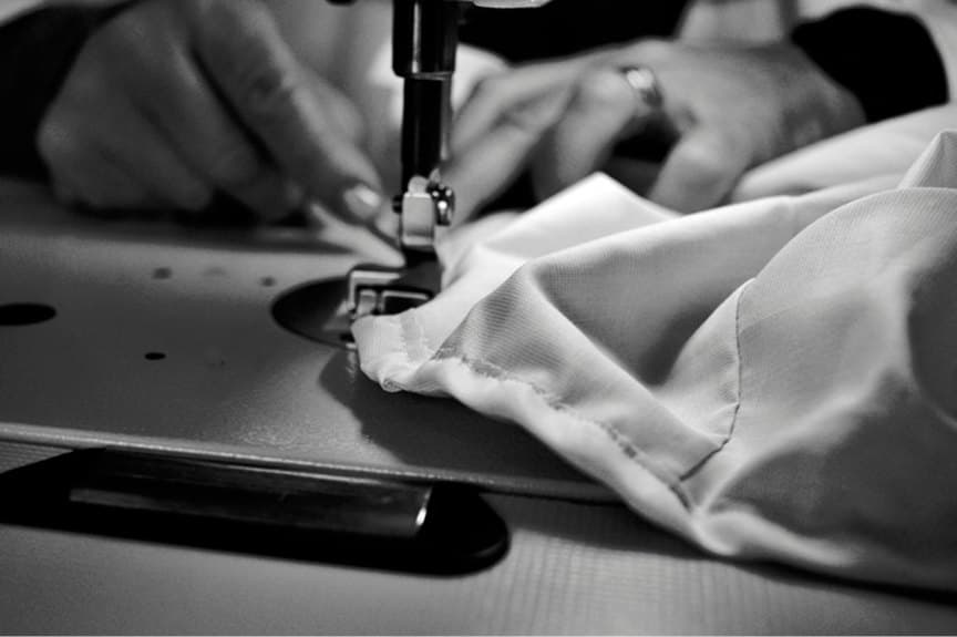 Black-and-white close-up of hands guiding fabric through a sewing machine