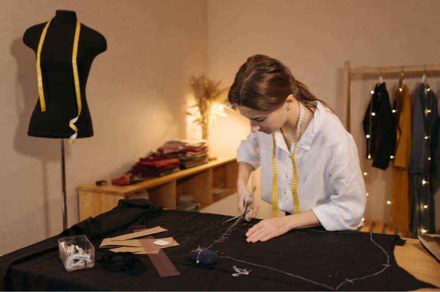 Seamstress cutting chalk-marked cloth at the atelier workbench