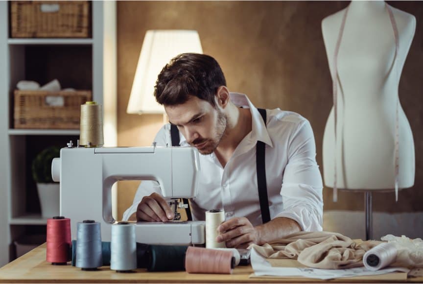Tailor working at a sewing machine beside a dress form in the atelier