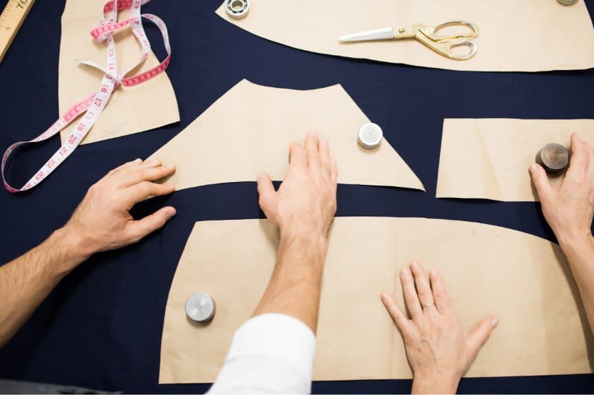 Tailors arranging paper pattern pieces on navy suiting cloth