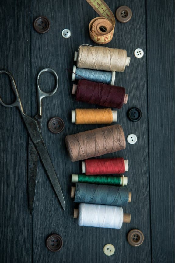 Spools of coloured thread, buttons and antique scissors on dark wood